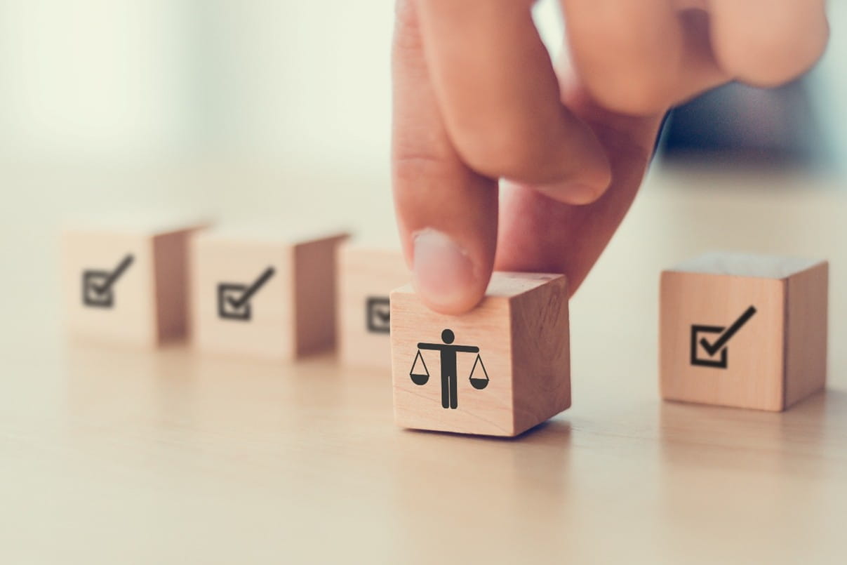 Hand moving a wooden block with a fairness symbol forward among checklist blocks, representing the Workplace Fairness Act and fair employment practices.